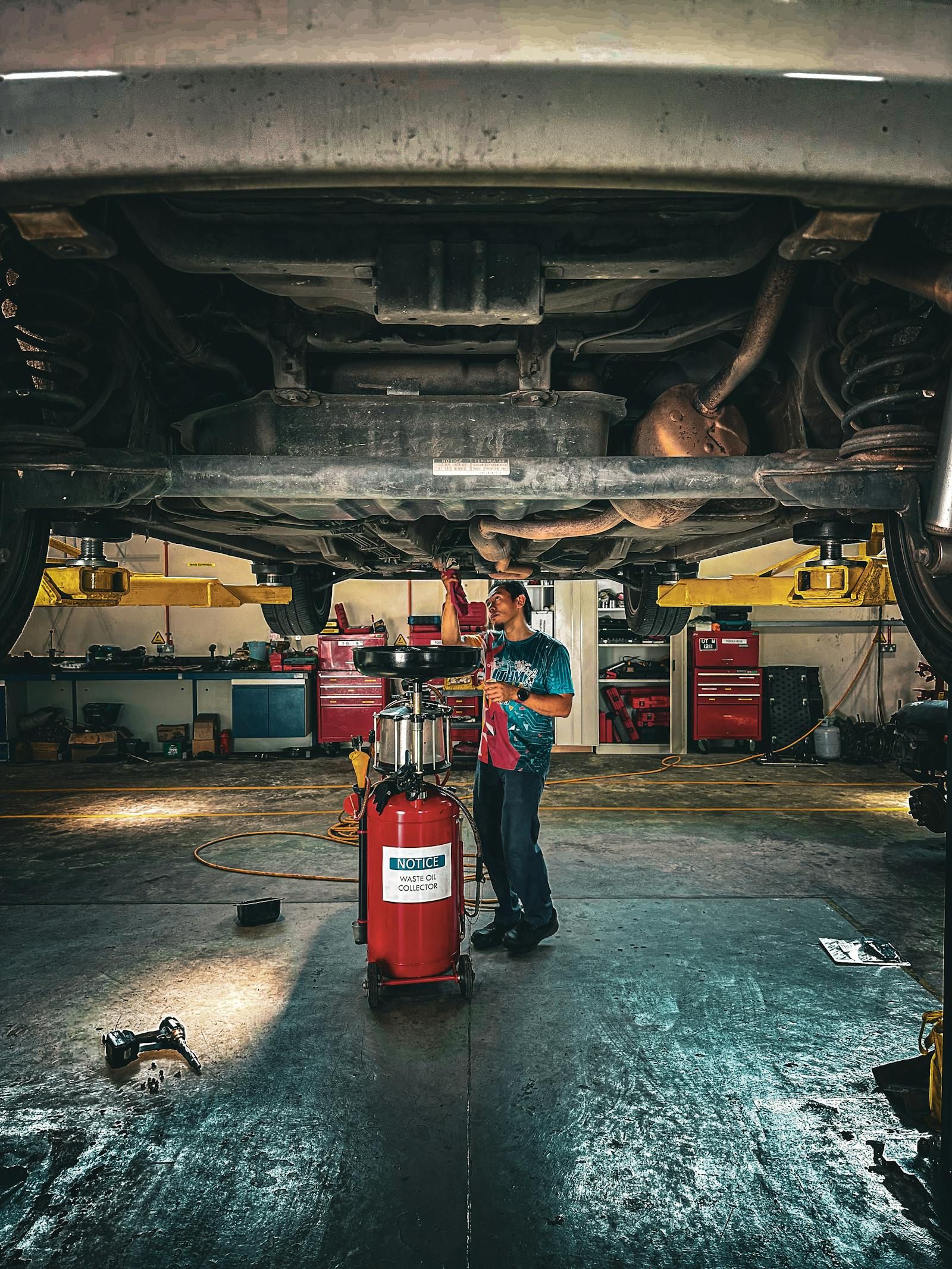 A mechanic working underneath a vehicle raised on a lift in an auto repair shop
