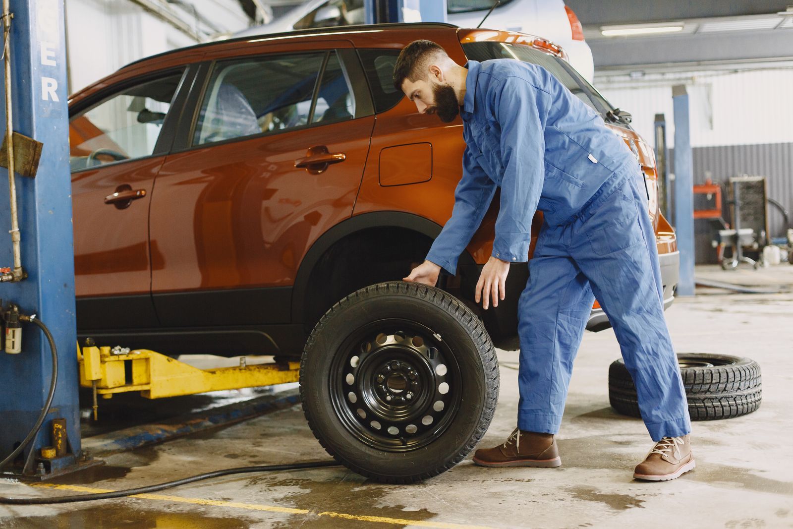 A mechanic removing a wheel from a vehicle raised on a shop lift