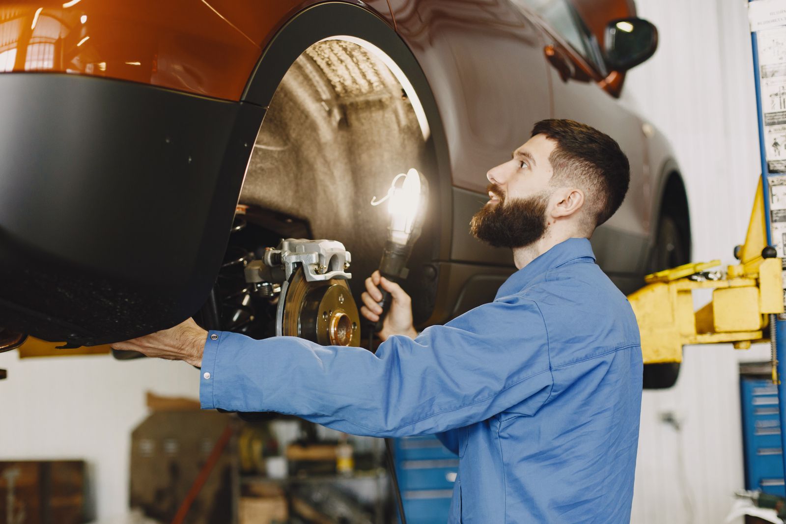 A mechanic inspecting a brake disc on a raised vehicle with a work light