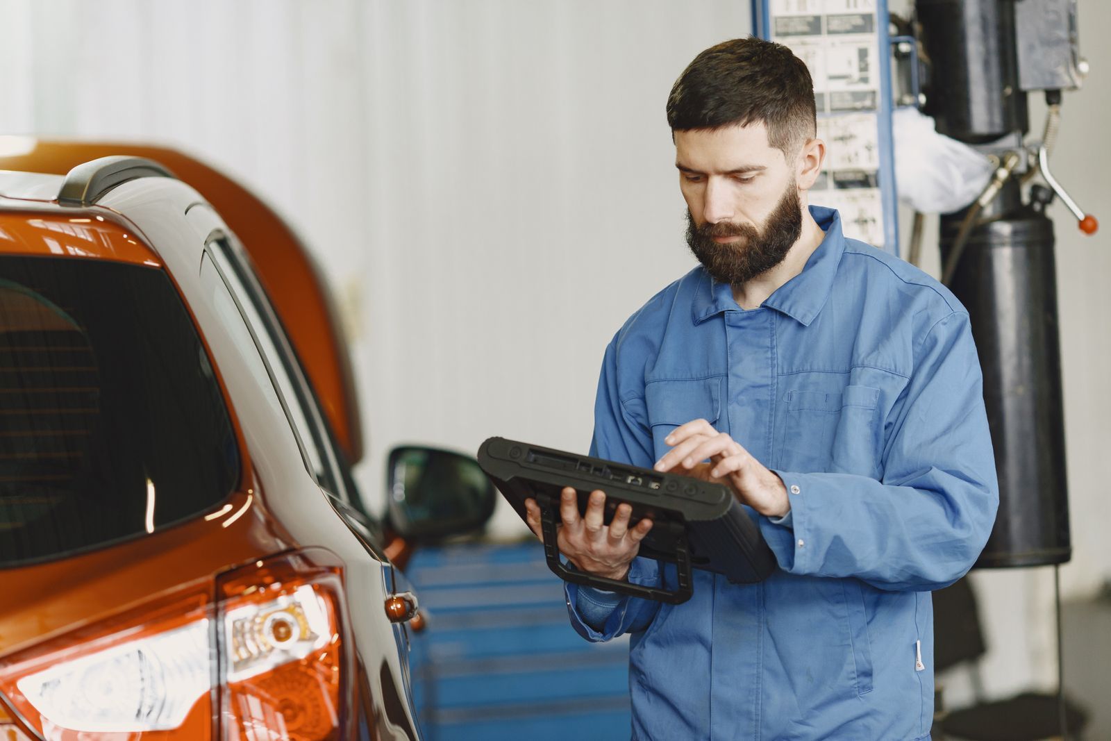 A mechanic using a handheld automotive diagnostic tool beside a car